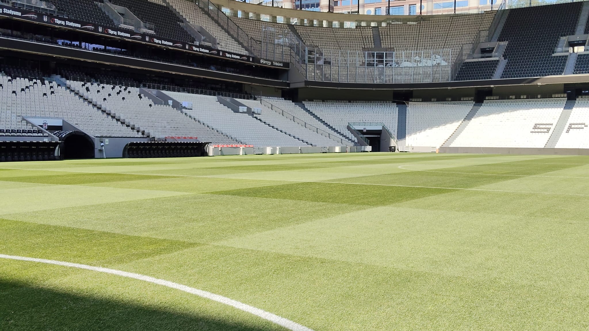 Empty sports stadium with a neatly mown green grass field and rows of seating.