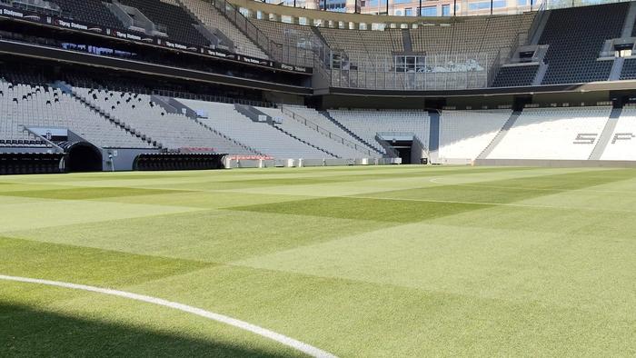 Empty sports stadium with a neatly mown green grass field and rows of seating.