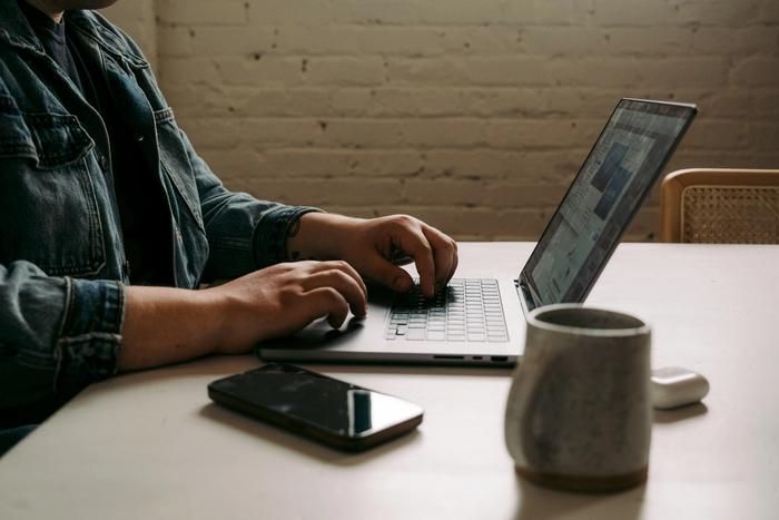 a man is sitting at a table typing on a laptop computer .