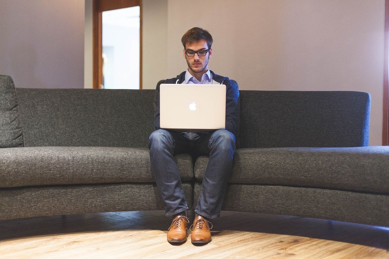 Um homem está sentado em um sofá usando um laptop.