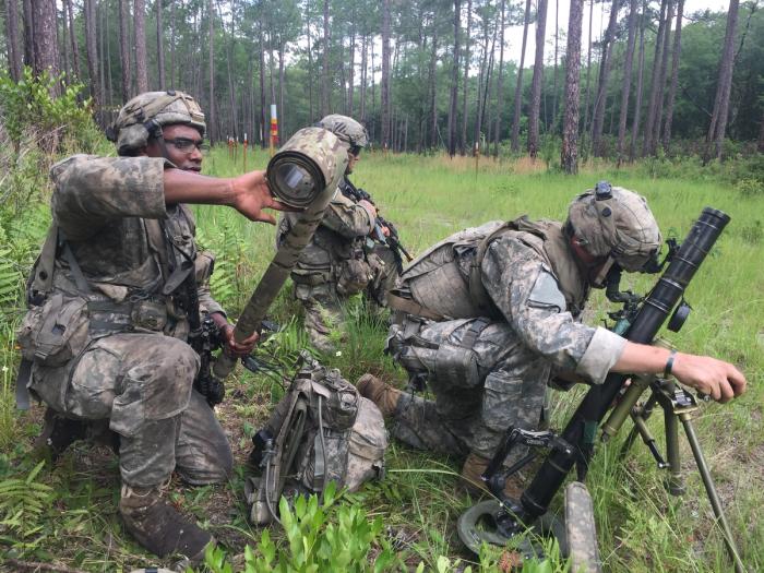 a group of soldiers are kneeling down in a field with a mortar .