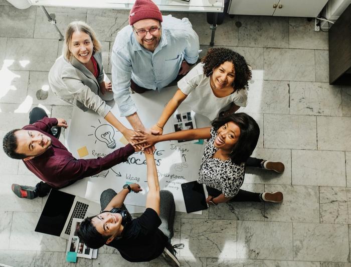 A group of people are sitting around a table putting their hands together.