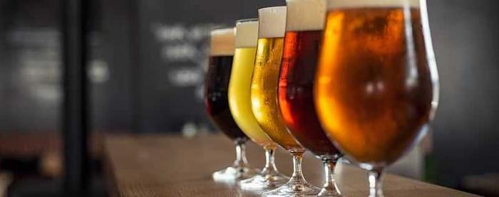 a row of glasses filled with different types of beer are lined up on a bar .