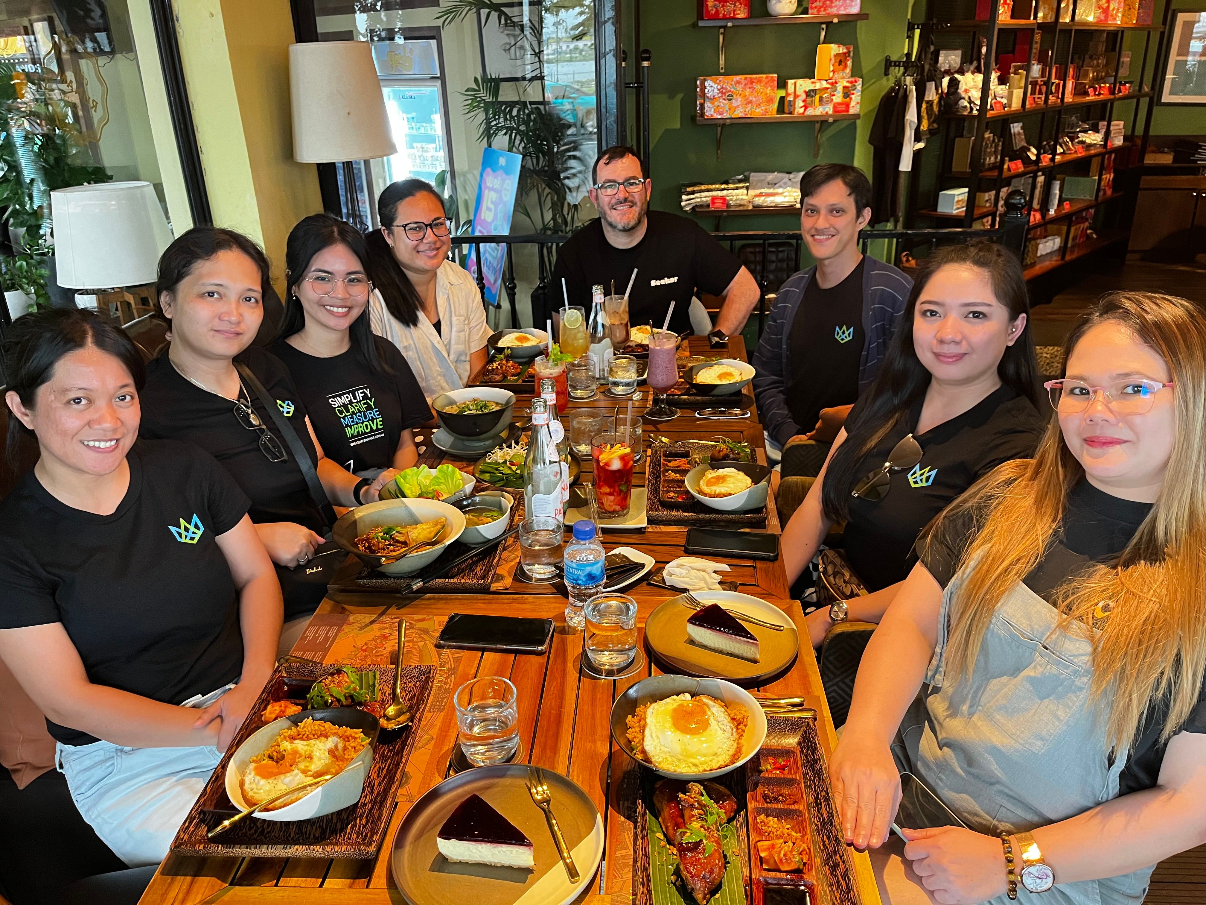 Ocho personas de Integration Kings, sonriendo mientras están sentadas alrededor de una mesa de restaurante llena de varios platos y bebidas.