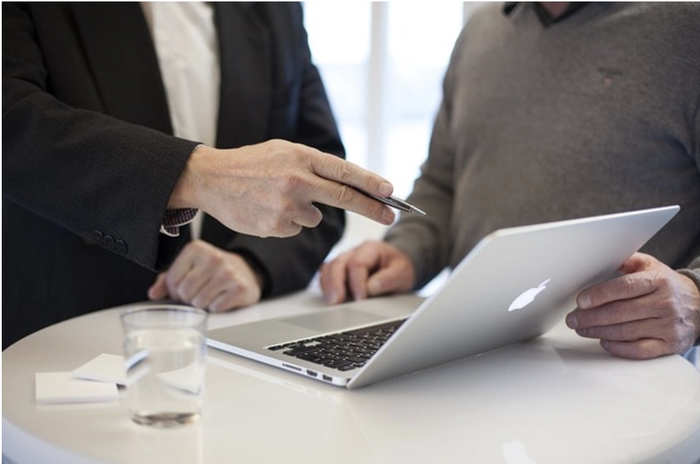 a man holding a pen pointing at an apple laptop