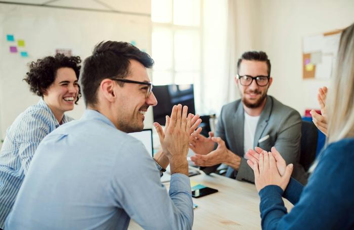 a group of people are sitting around a table clapping their hands .