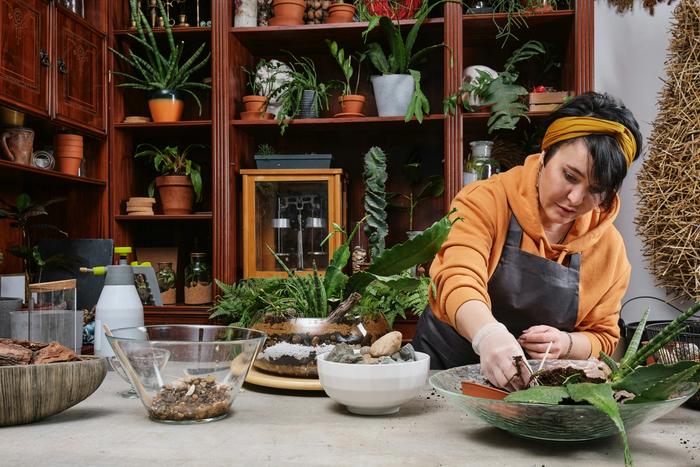 a woman is sitting at a table making a terrarium with plants .