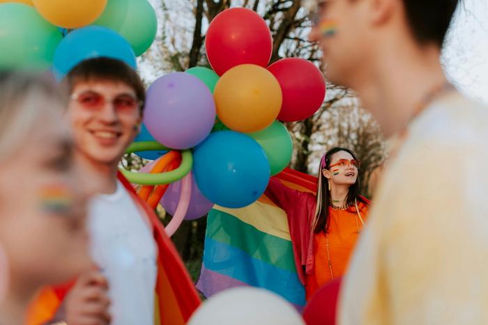 a group of people are holding balloons and a rainbow flag .