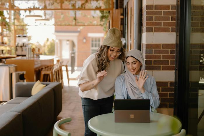 two women are sitting at a table looking at a laptop computer .