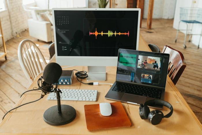a desk with a computer , microphone , laptop and headphones on it .