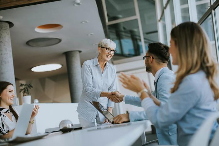 a group of business people are sitting around a table shaking hands .