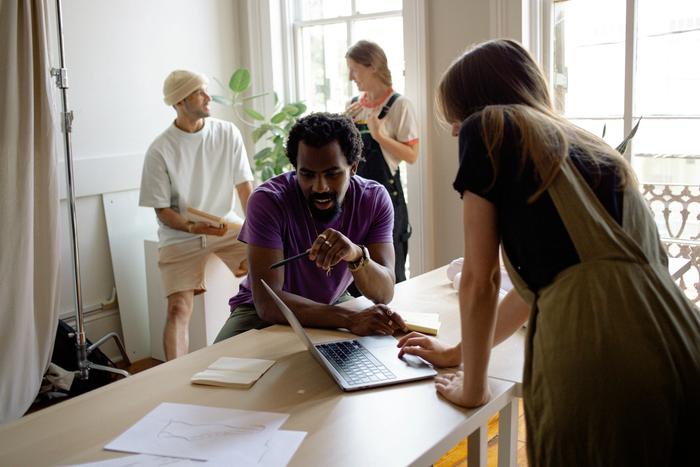 a group of people are sitting at a table looking at a laptop computer .