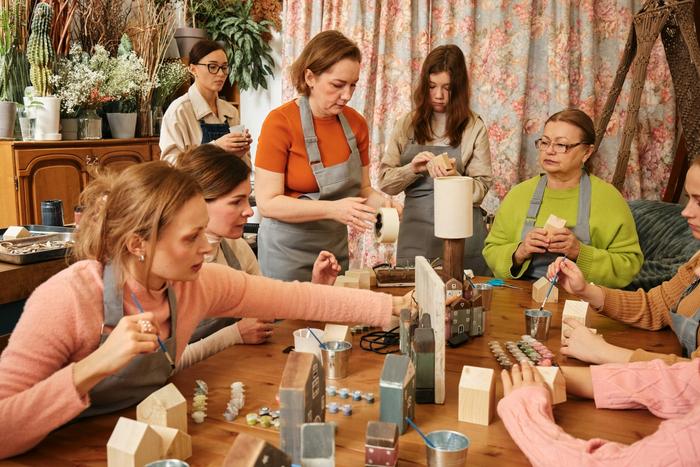 a group of women are sitting around a table making candles .