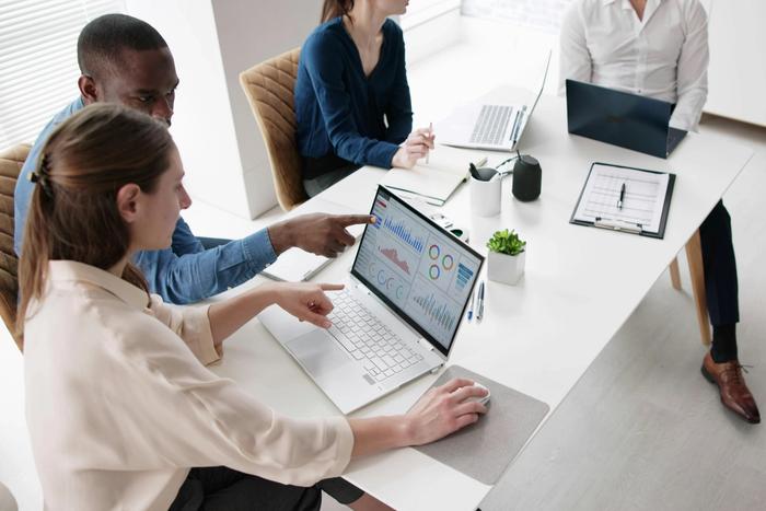 a group of people are sitting around a table with laptops .