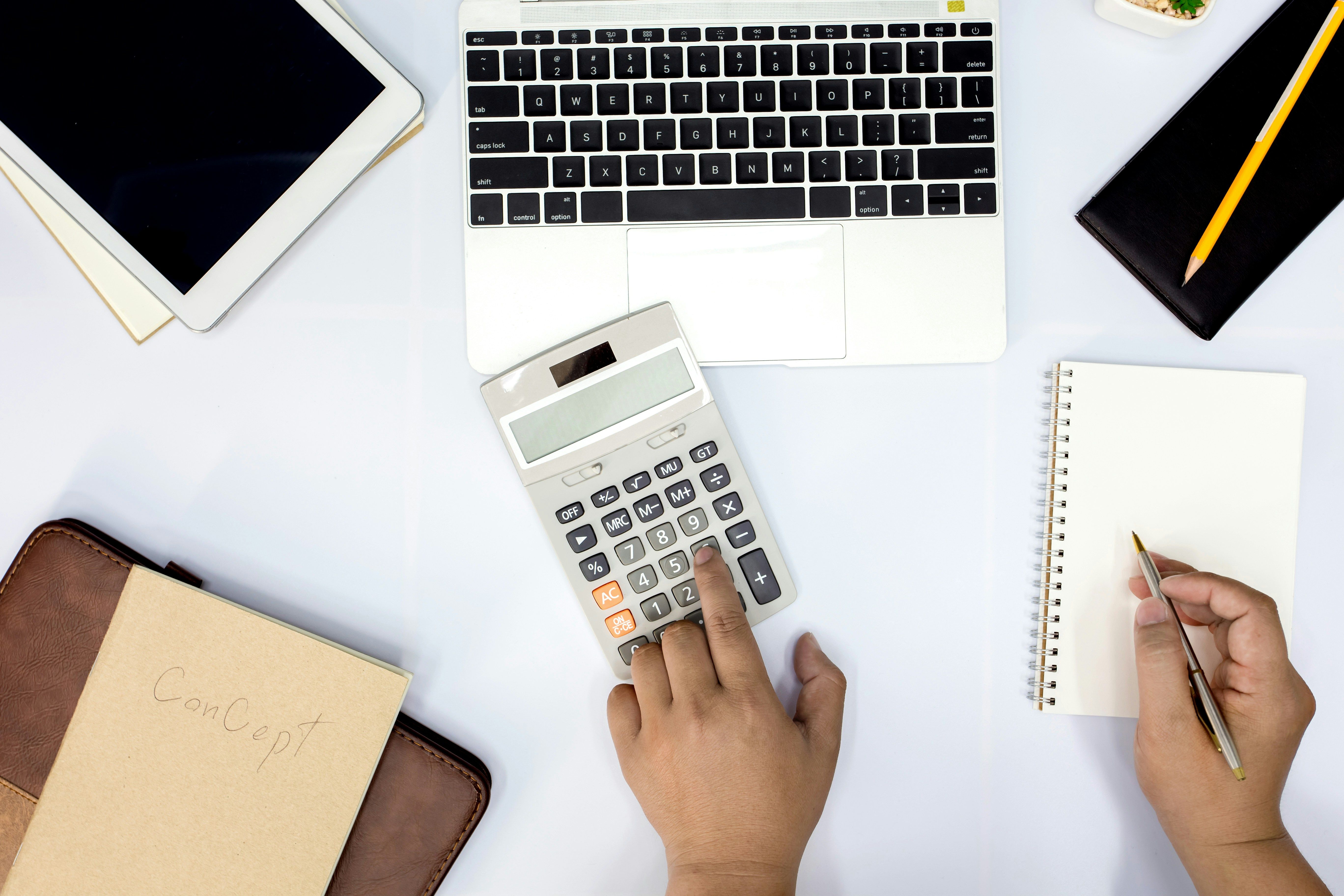 a person is using a calculator and writing in a notebook .