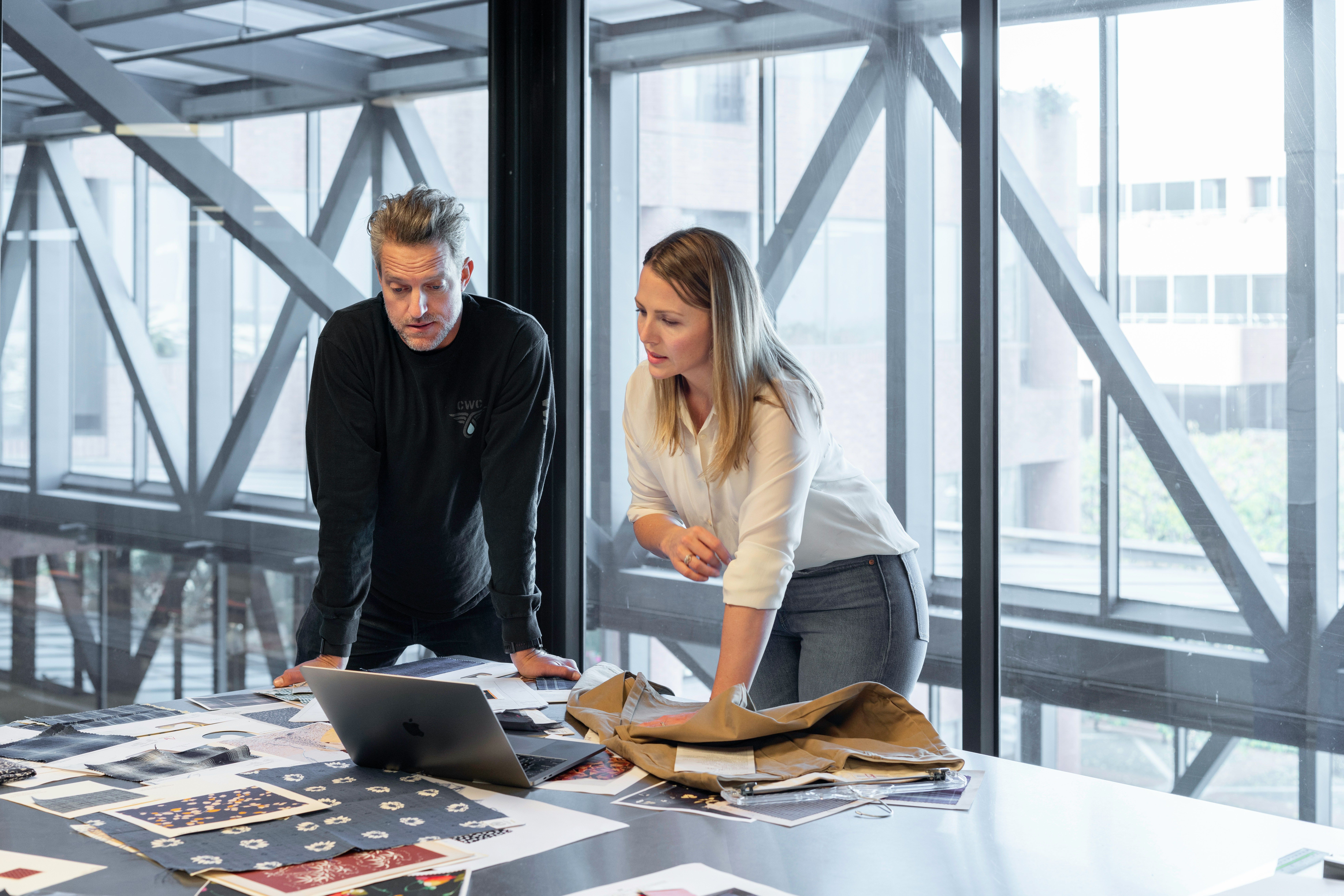 a man and a woman are looking at a laptop on a table .