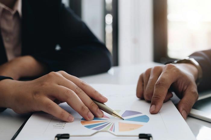 a man and a woman are looking at a pie chart on a clipboard .