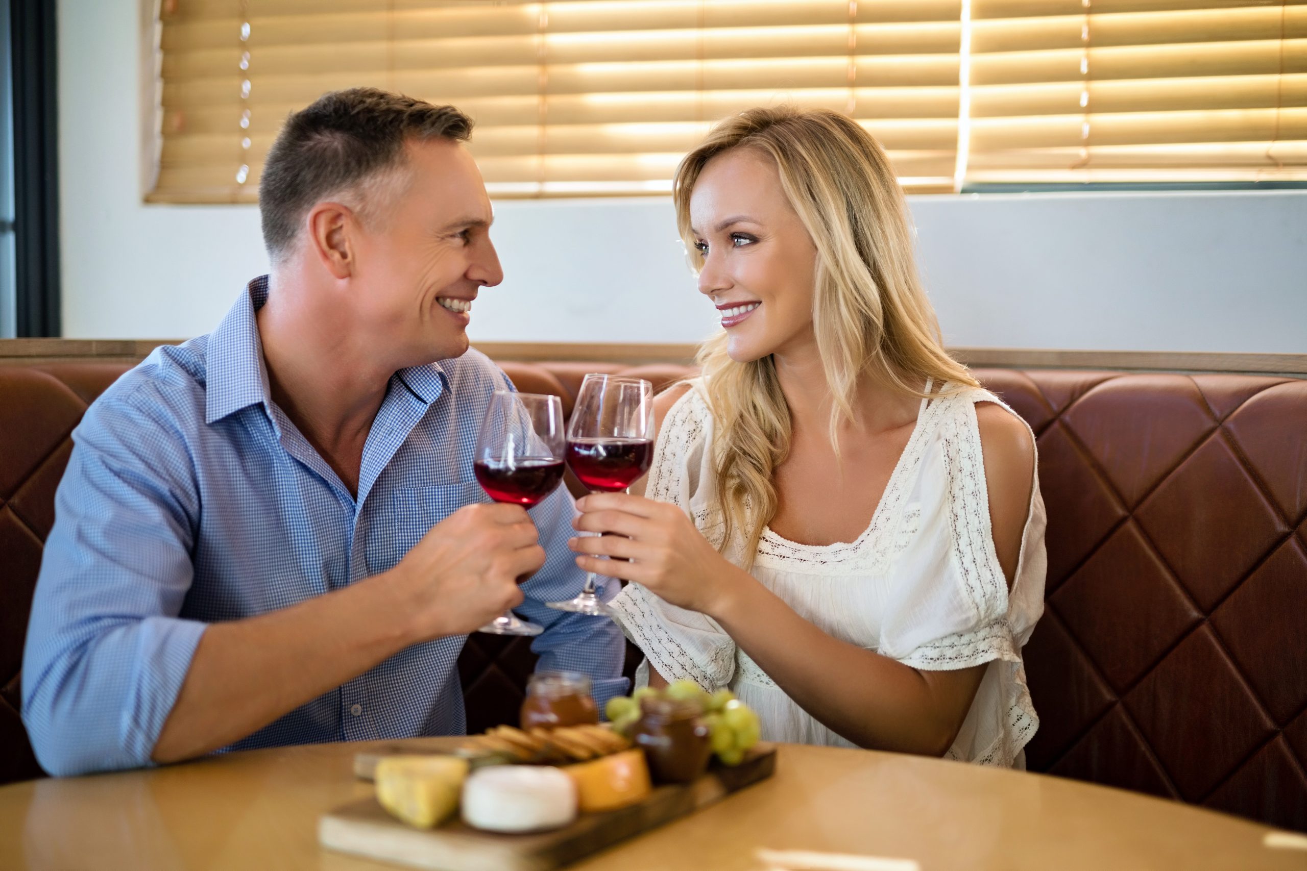 Couple clinking glasses of red wine over a cheese board