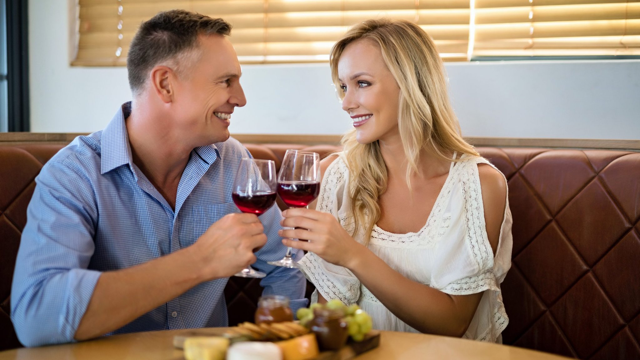 Couple clinking glasses of red wine over a cheese board