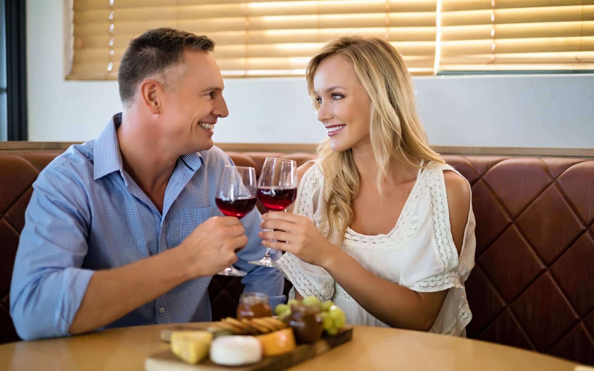 Couple clinking glasses of red wine over a cheese board