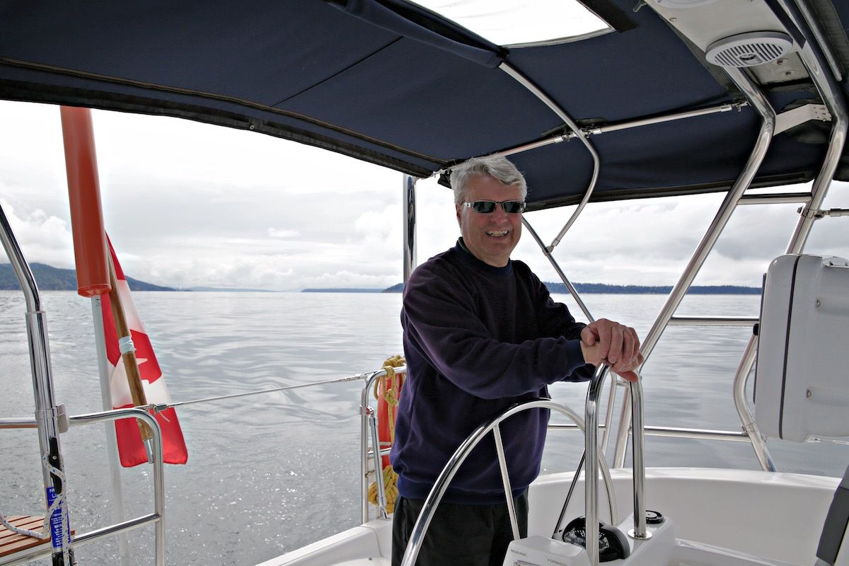 Man wearing sunglasses steers a sailboat on calm water
