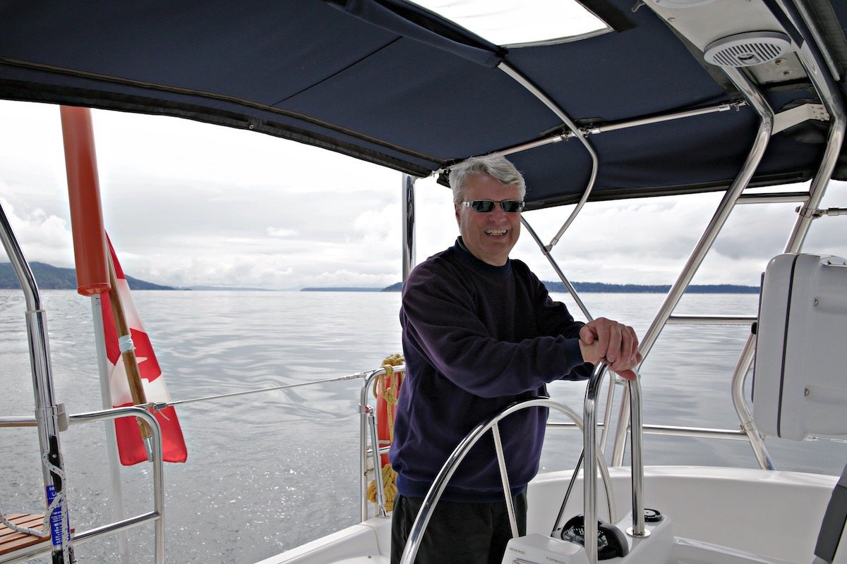 Man wearing sunglasses steers a sailboat on calm water