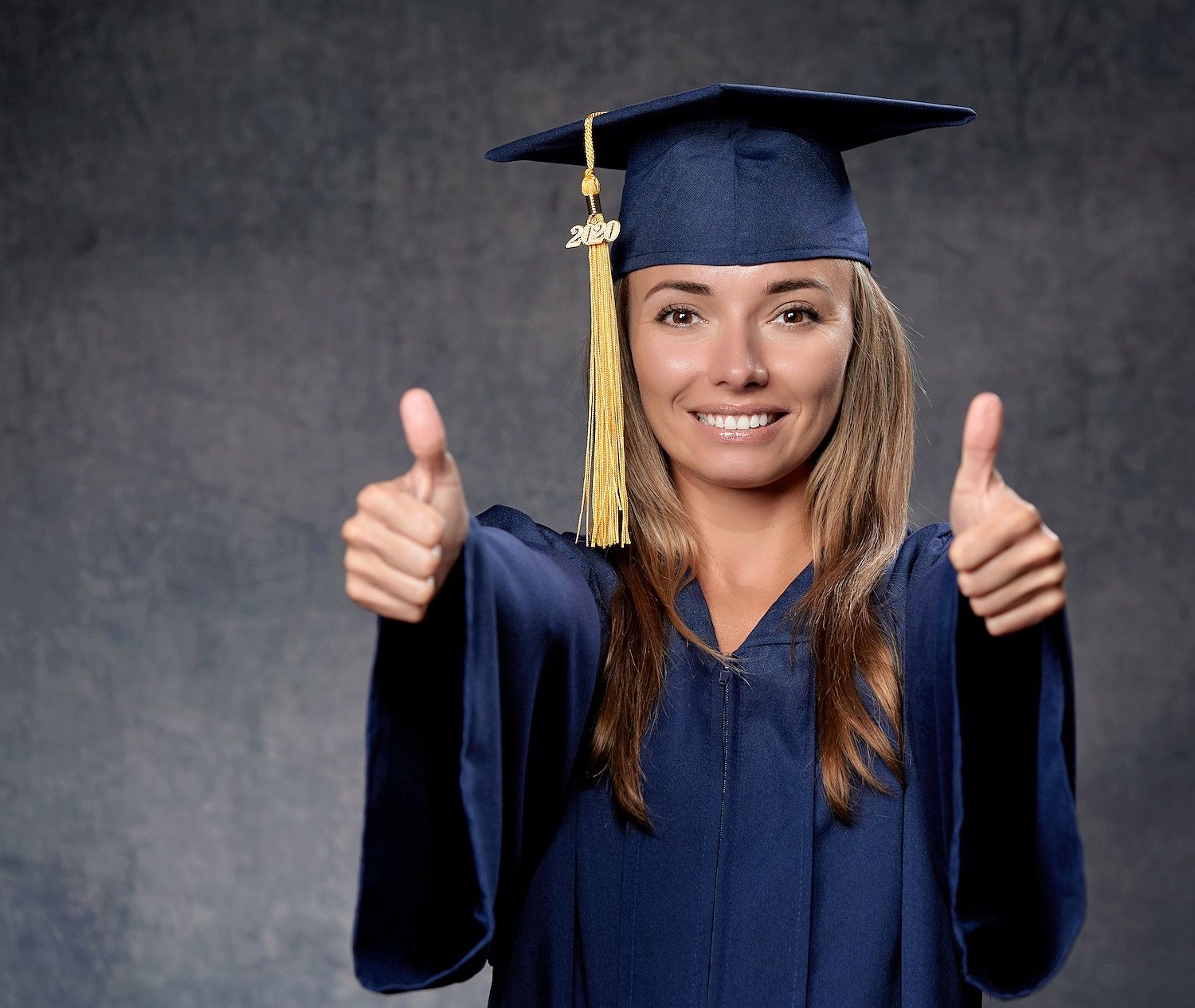 Graduate in cap and gown gives two thumbs up