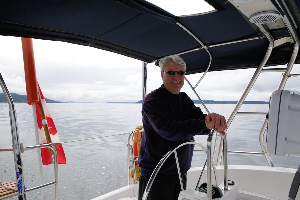 Man wearing sunglasses steers a sailboat on calm water