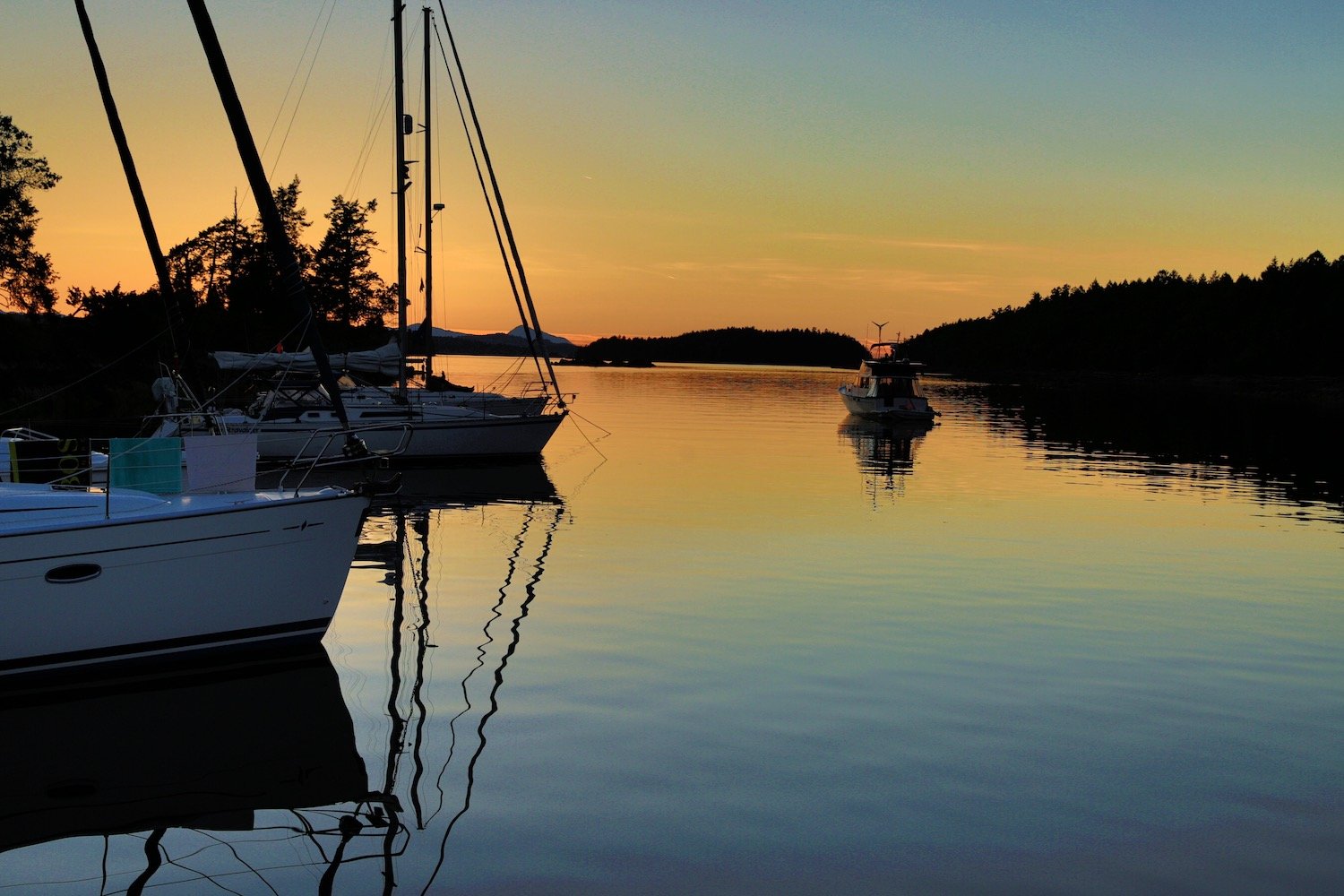 Sailboats moored on calm water as a motorboat passes at sunset