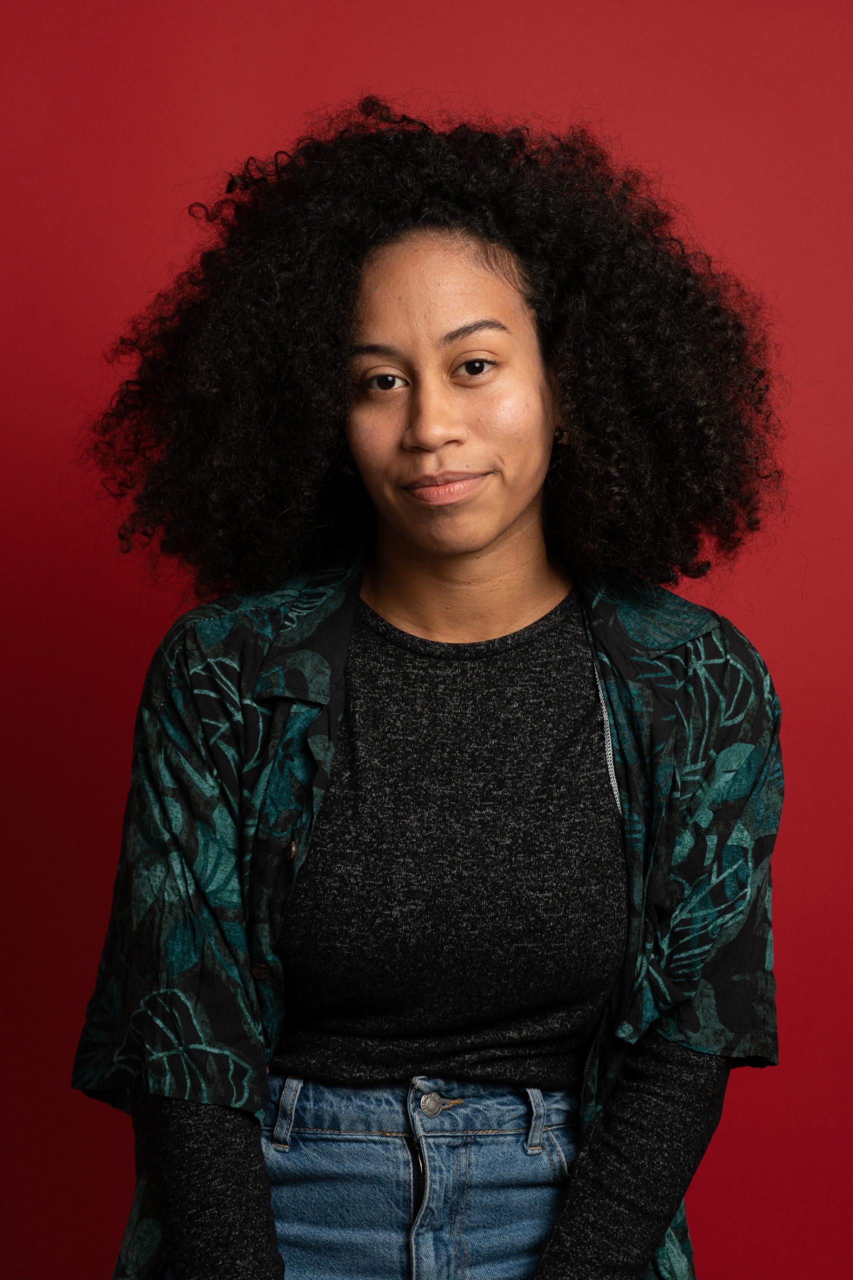 Woman with curly hair facing the camera against a red background