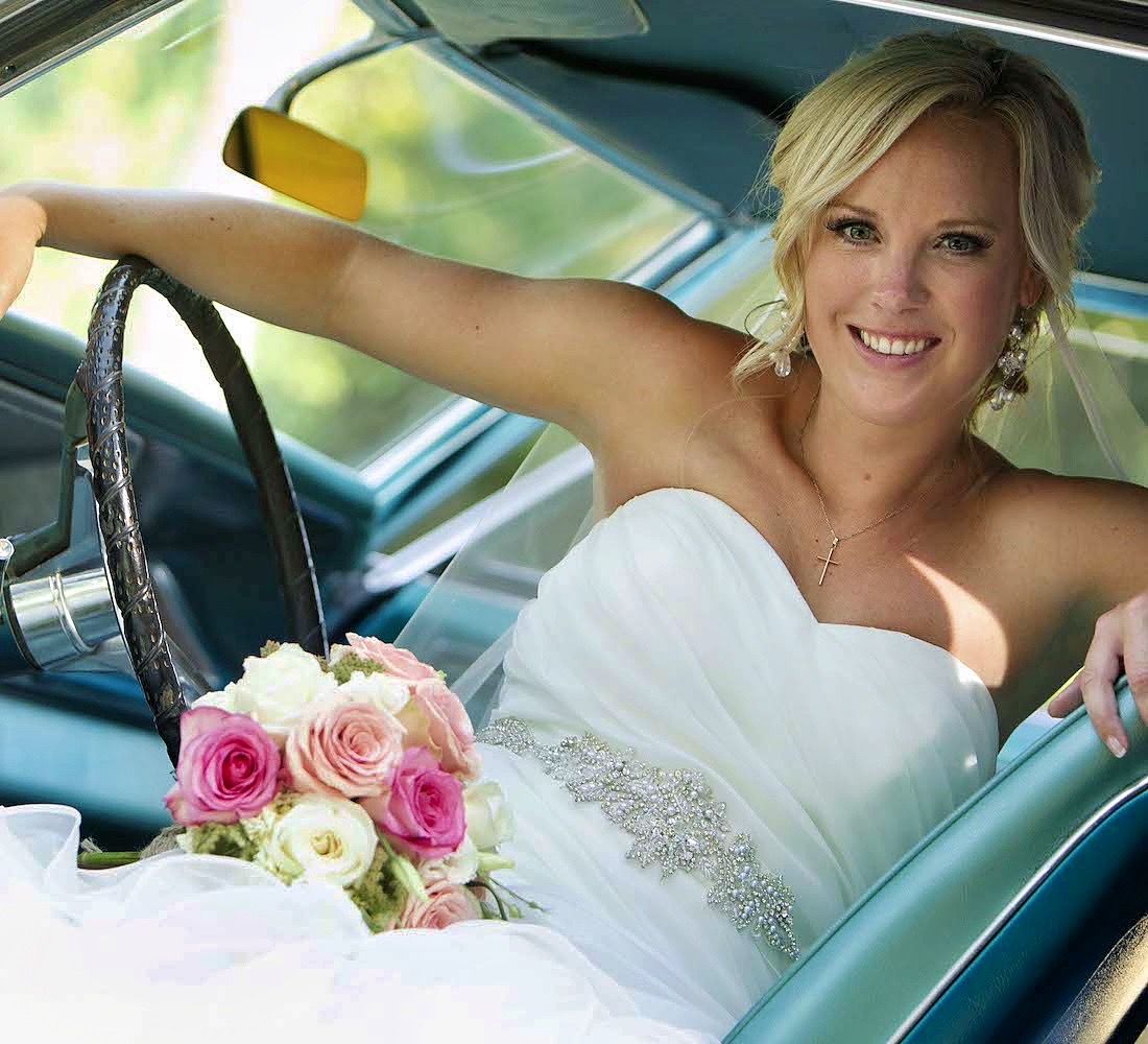 Bride holding a bouquet and smiling from the driver's seat