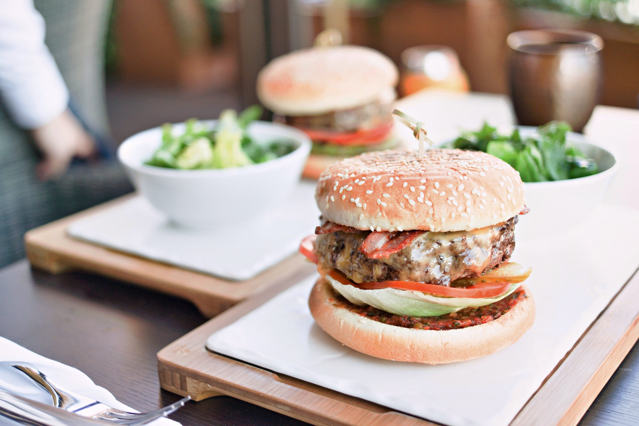 Cheeseburger with lettuce and tomato served alongside bowls of salad