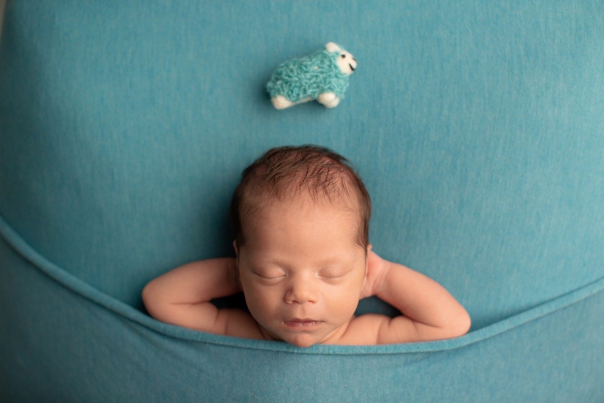Newborn baby sleeps with hands behind head beneath a toy sheep