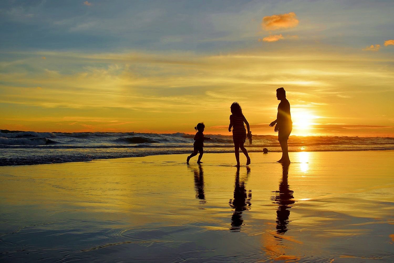 Adult and two children play at the shoreline during sunset