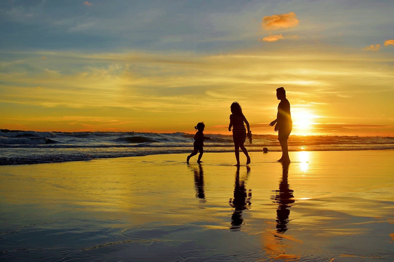 Adult and two children play at the shoreline during sunset