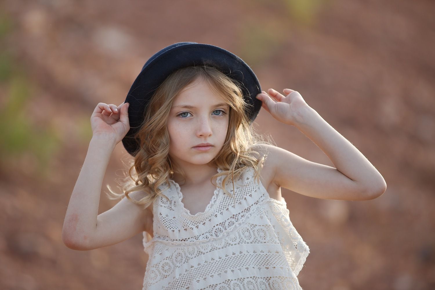 Young girl in a lace dress adjusts her black hat