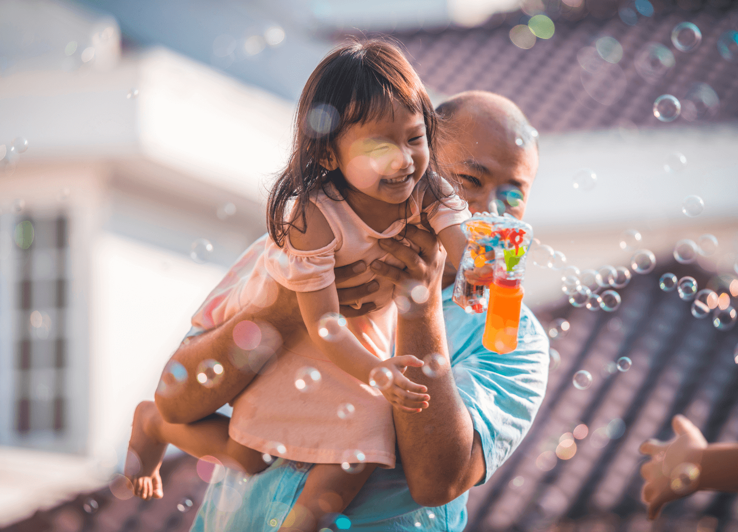 Father carries his smiling daughter as she blows bubbles