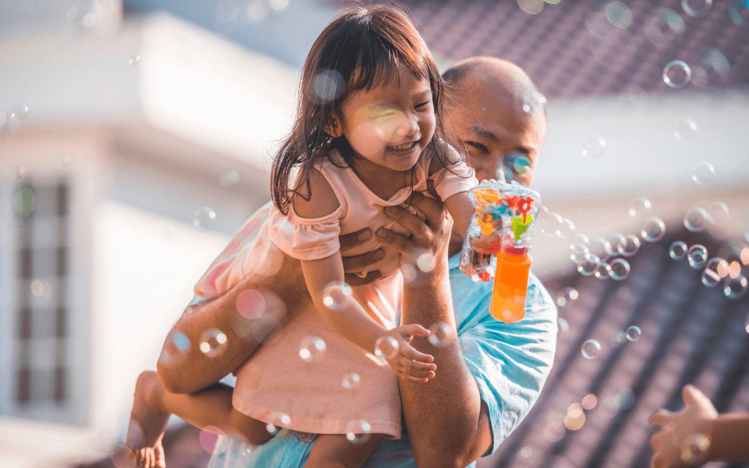 Father carries his smiling daughter as she blows bubbles