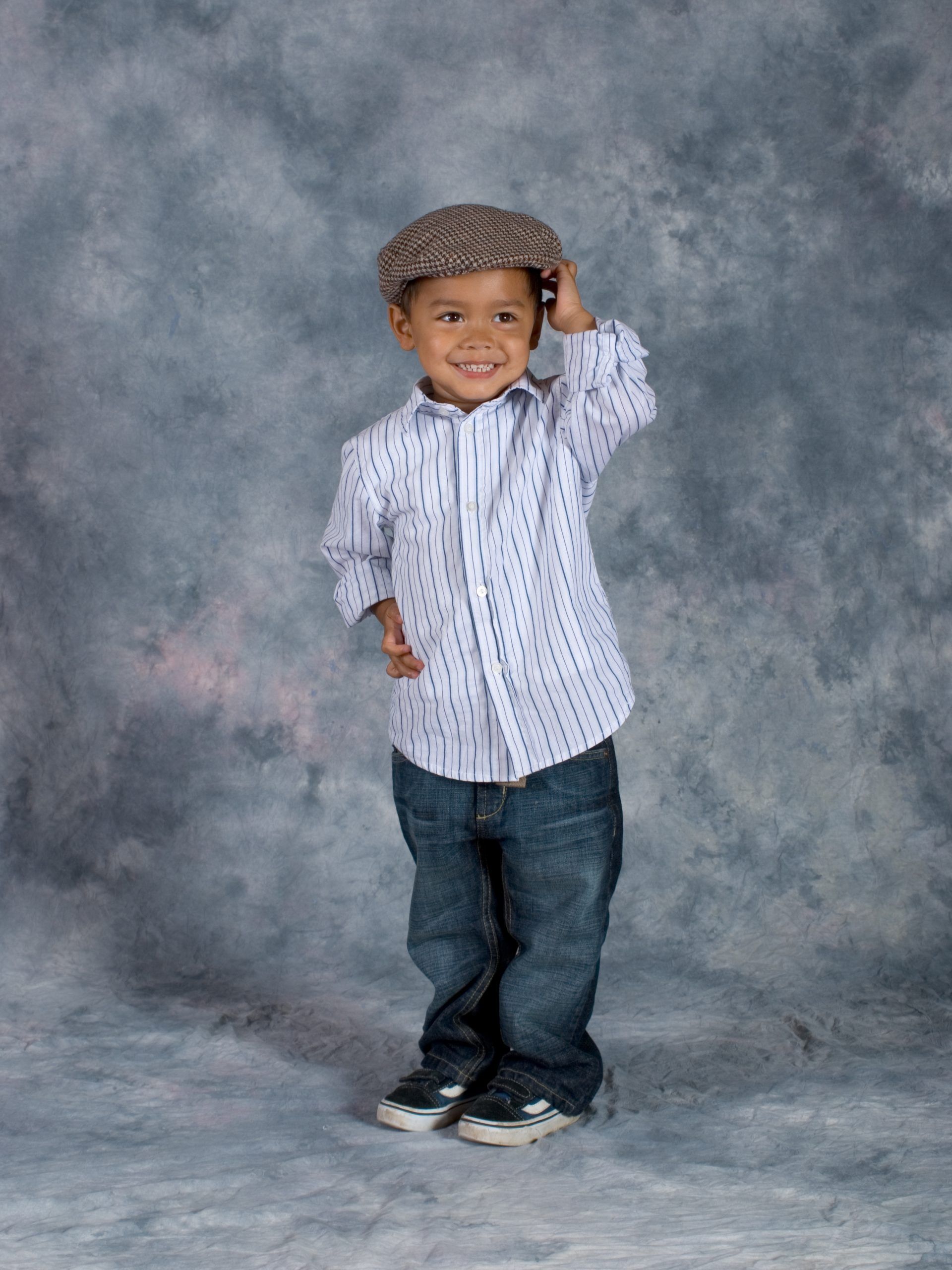 Smiling young boy poses while touching his flat cap
