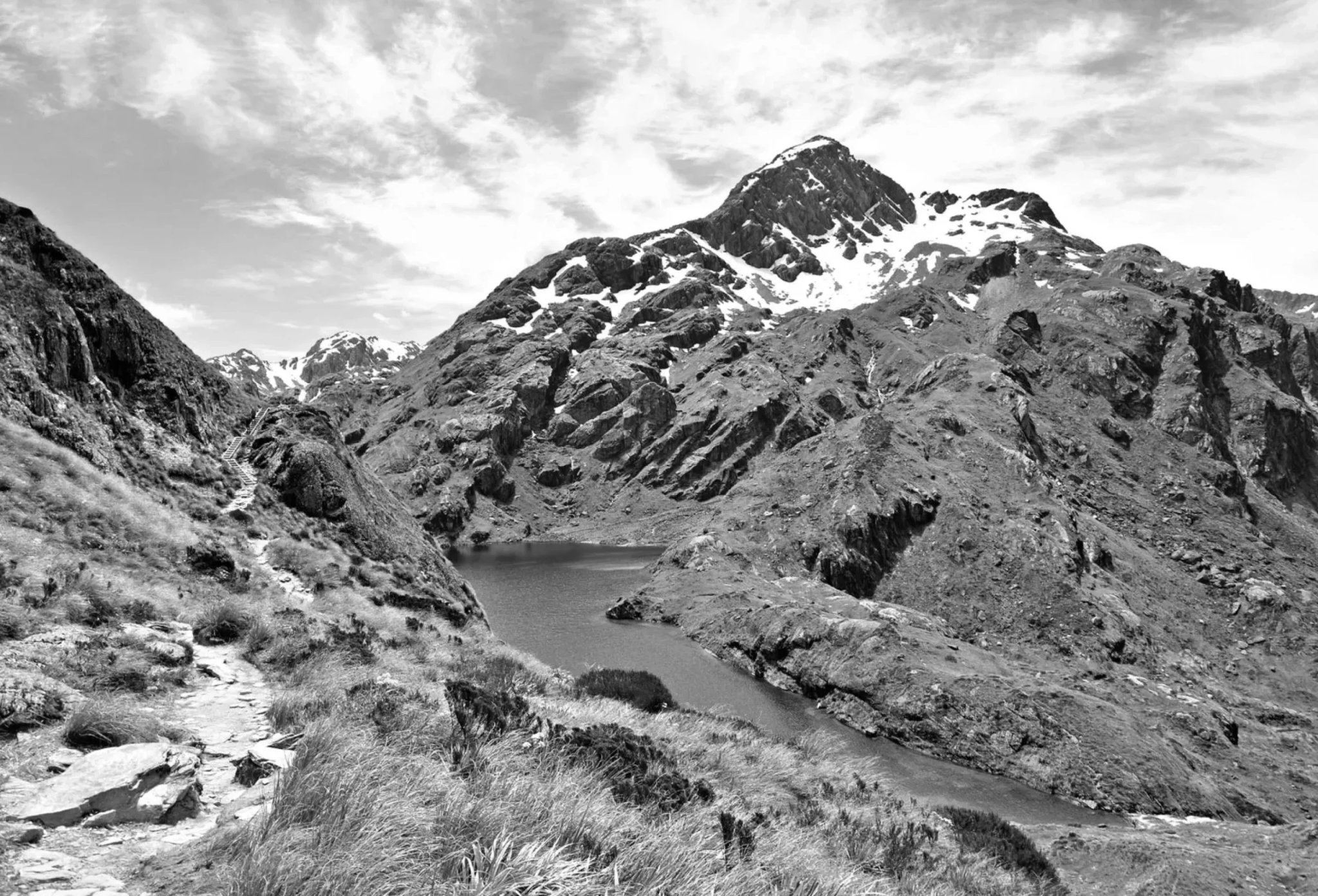 Snow-capped rocky mountains rise above a lake and hiking trail