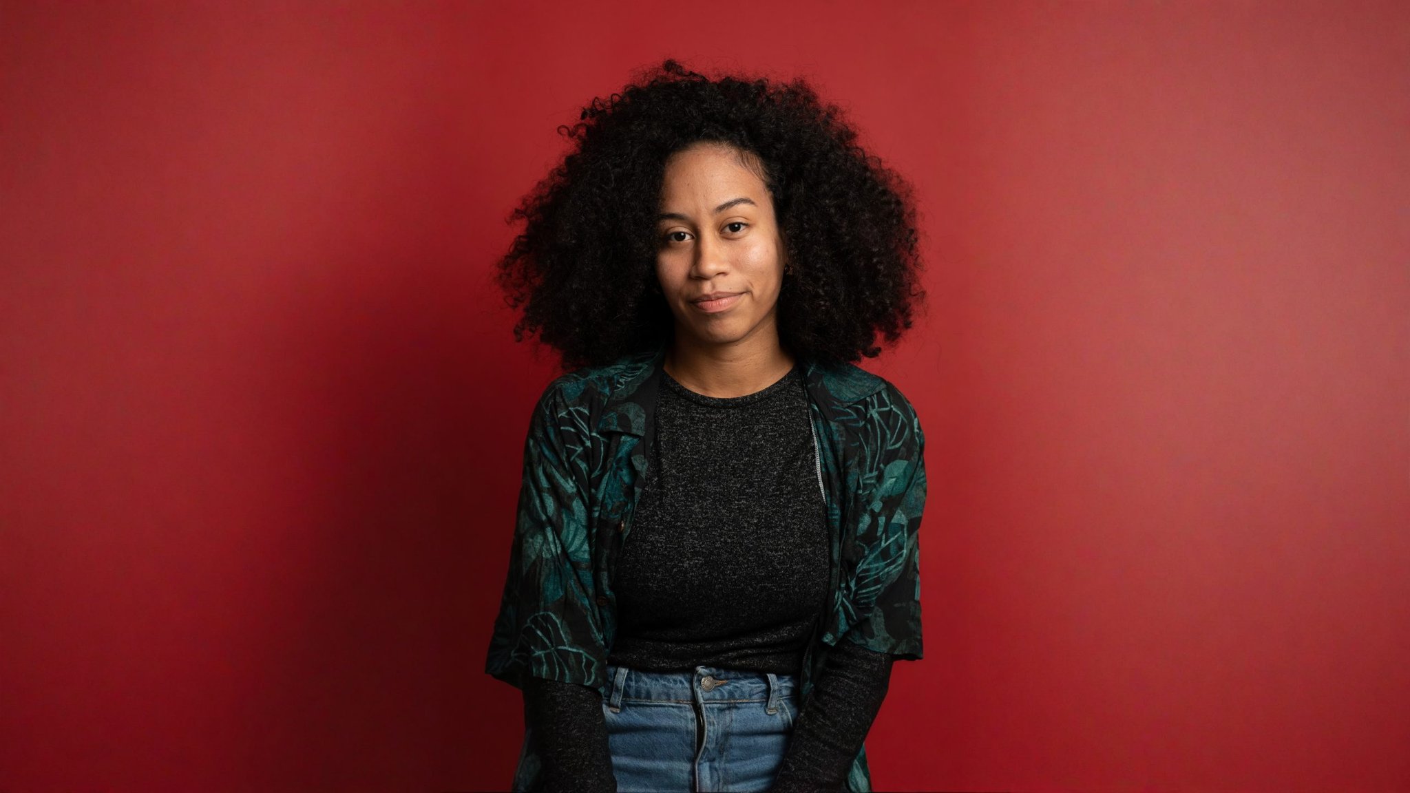 Woman with curly hair facing the camera against a plain backdrop