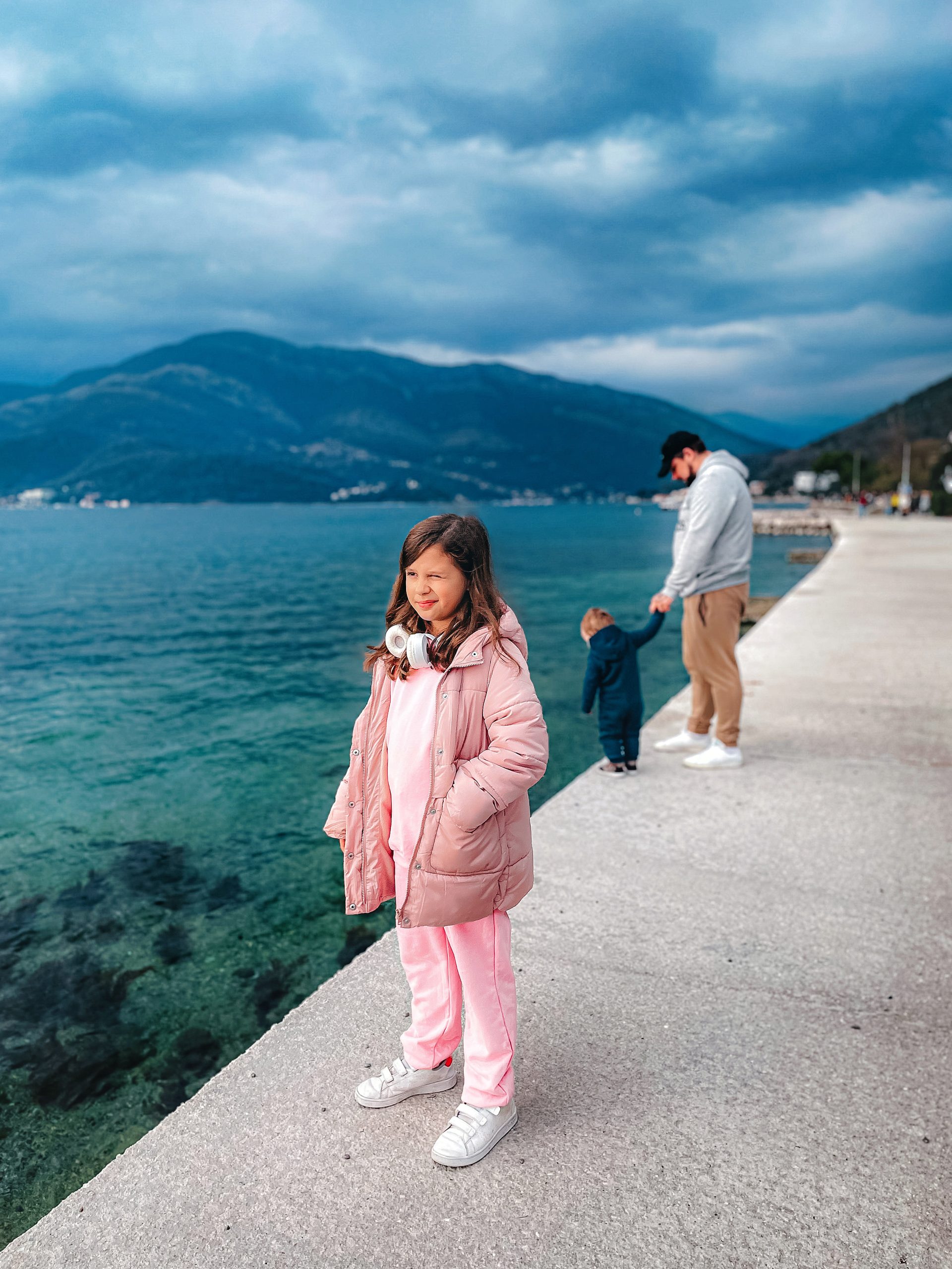 Girl stands on a waterfront pier with mountains across the bay