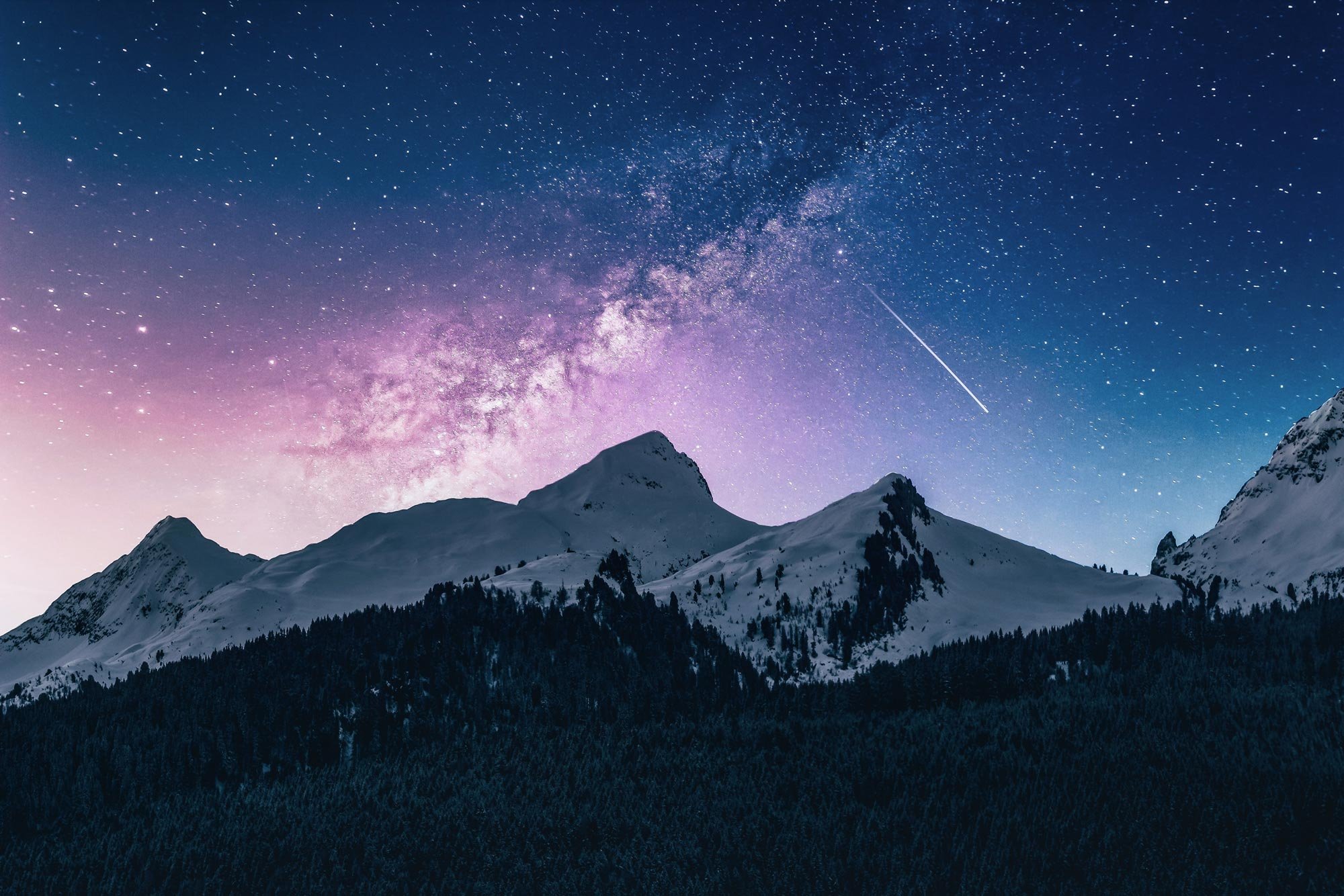 Snow-covered mountains beneath the Milky Way and a shooting star