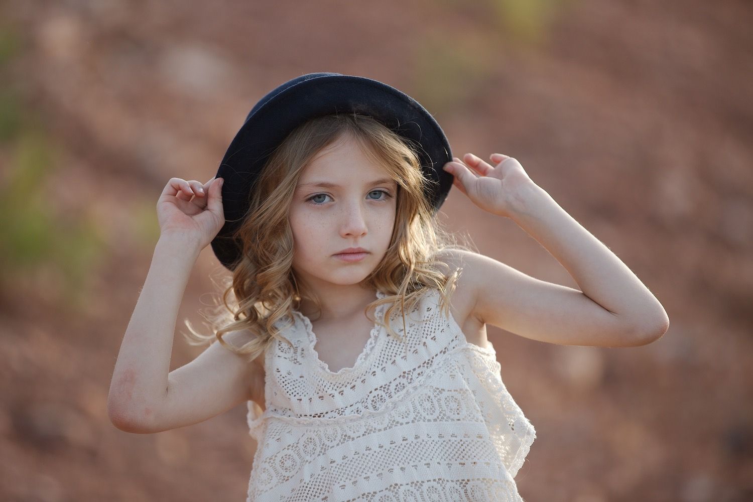 Young girl adjusts a black hat with both hands