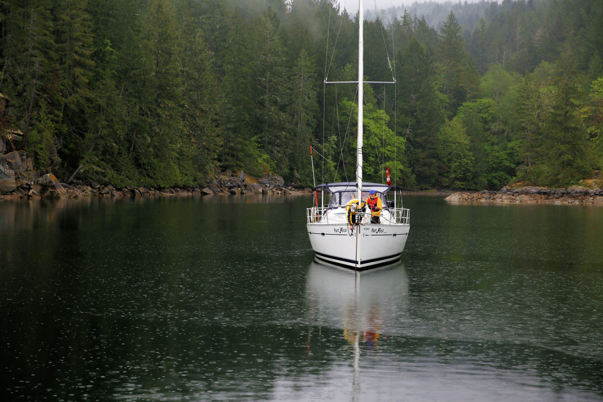 Sailboat carrying two people on a forest-lined inlet