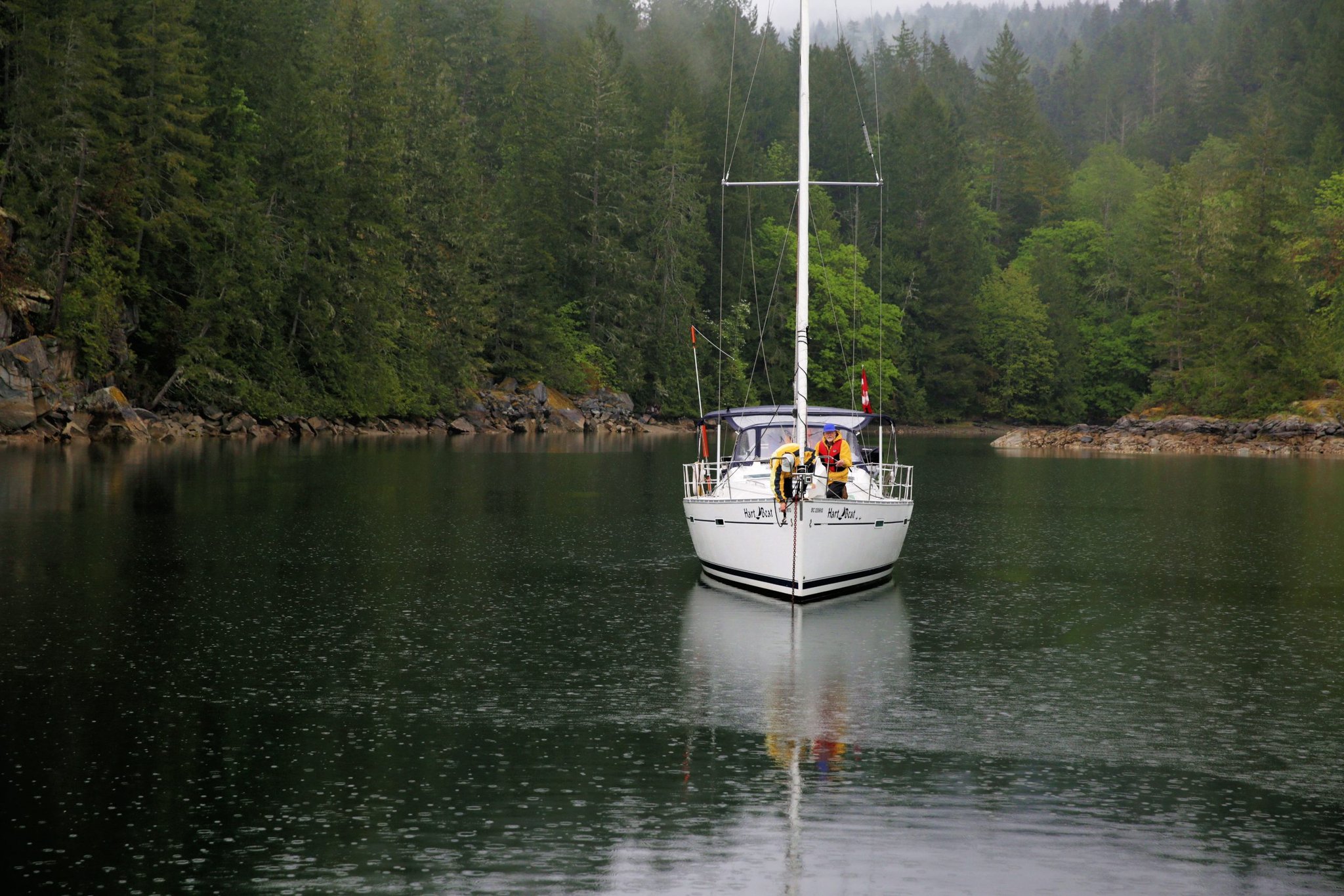 Sailboat carrying two people on a forest-lined inlet