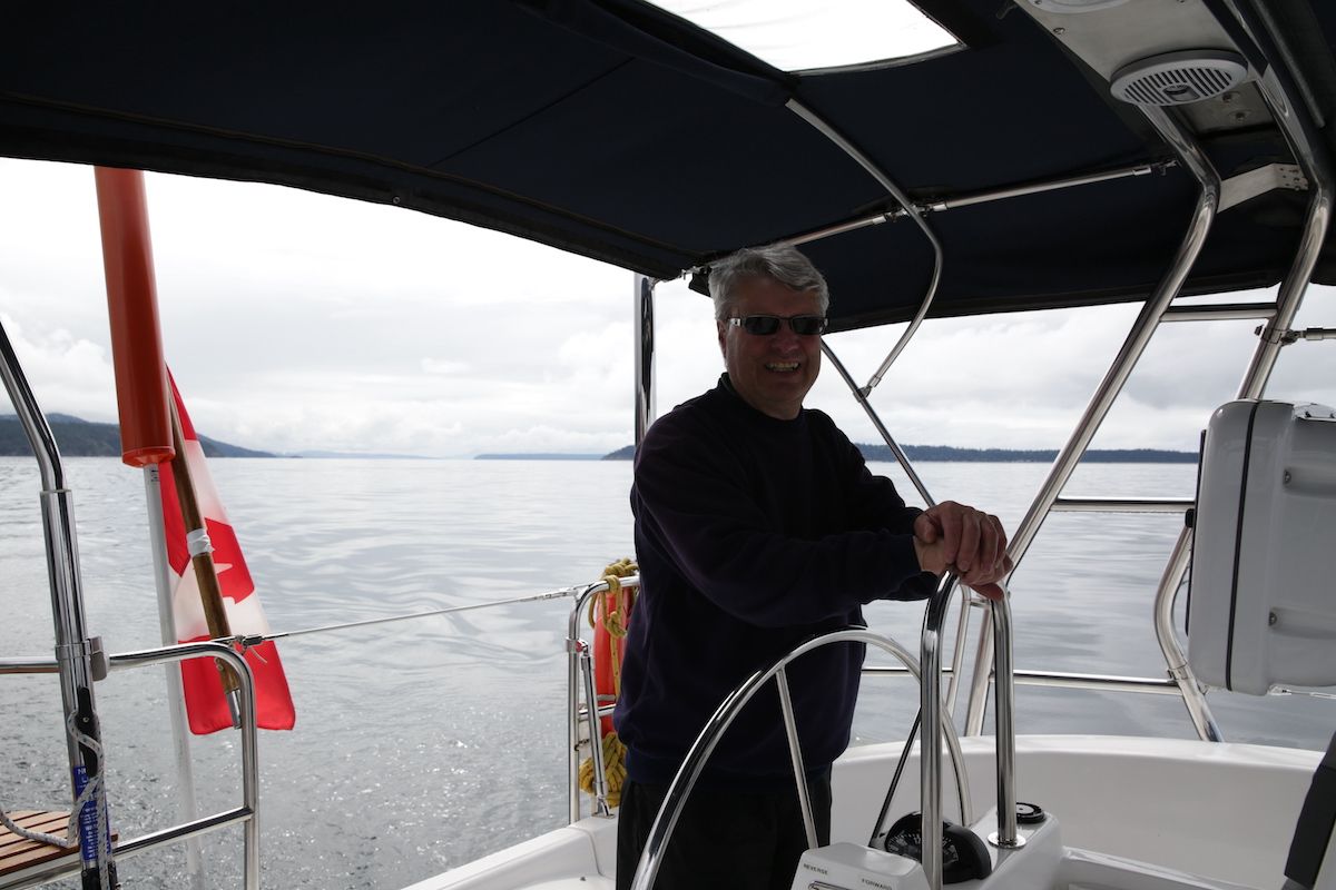 Man wearing sunglasses steers a sailboat on calm water