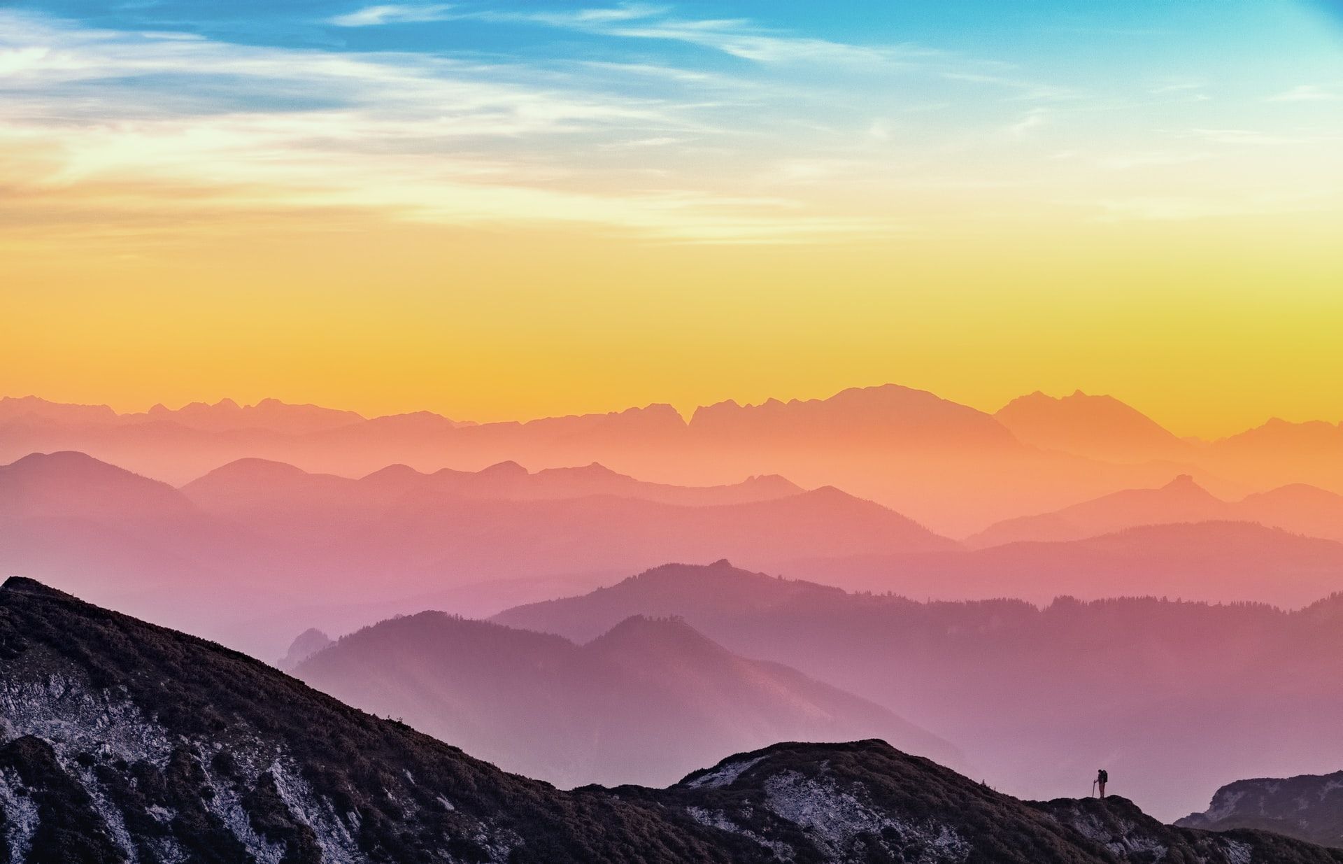 Lone hiker overlooks layered mountain ranges at sunset