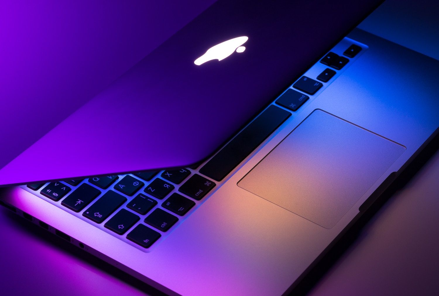 Partially open Apple laptop with illuminated logo, keyboard and trackpad