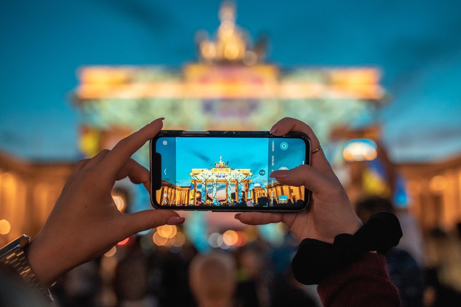 Person photographs the illuminated Brandenburg Gate with a smartphone